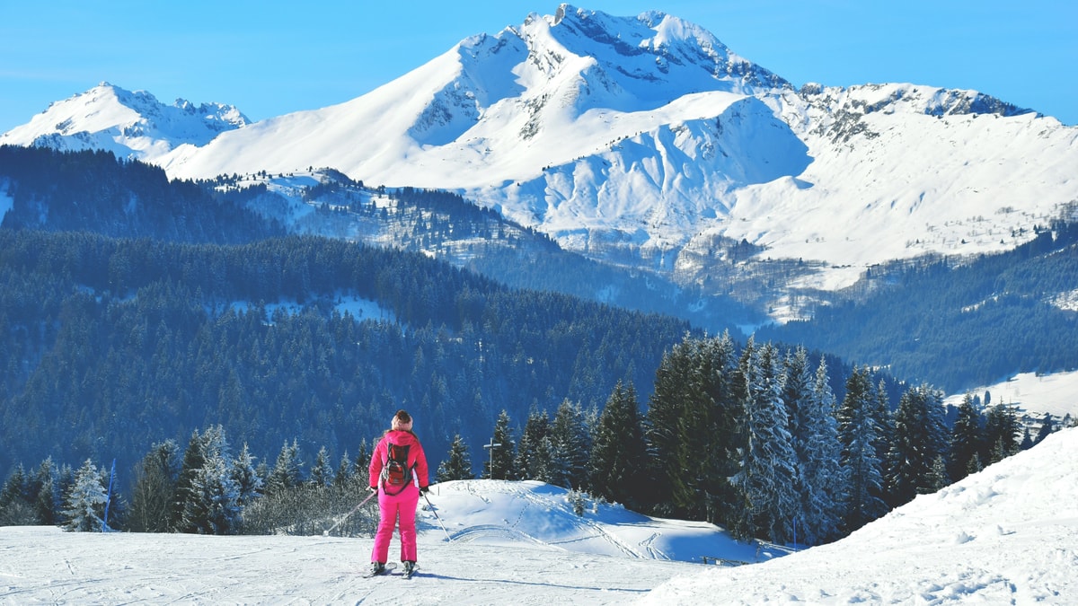 A skier in pink on a slope above Morzine, with snowy French Alps peaks beyond