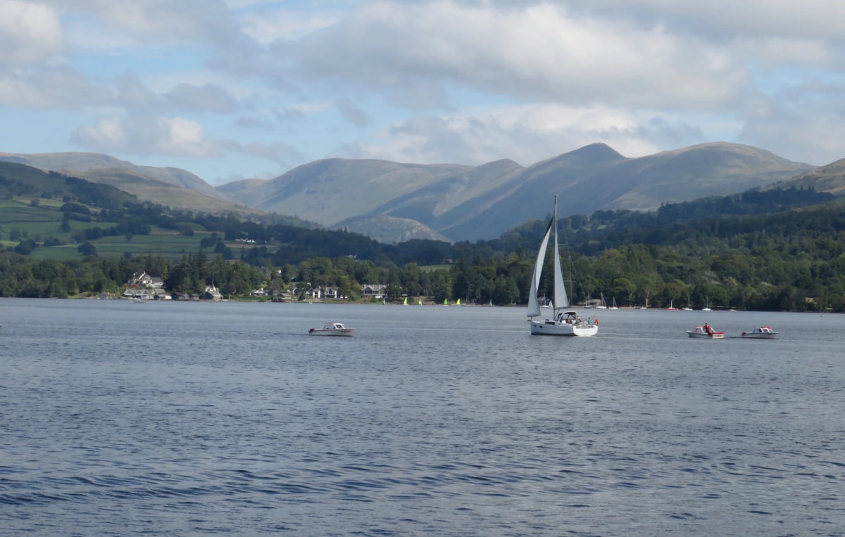 Sailing boat and motorboats on Windermere below the Lake District fells near Troutbeck Bridge, Cumbria