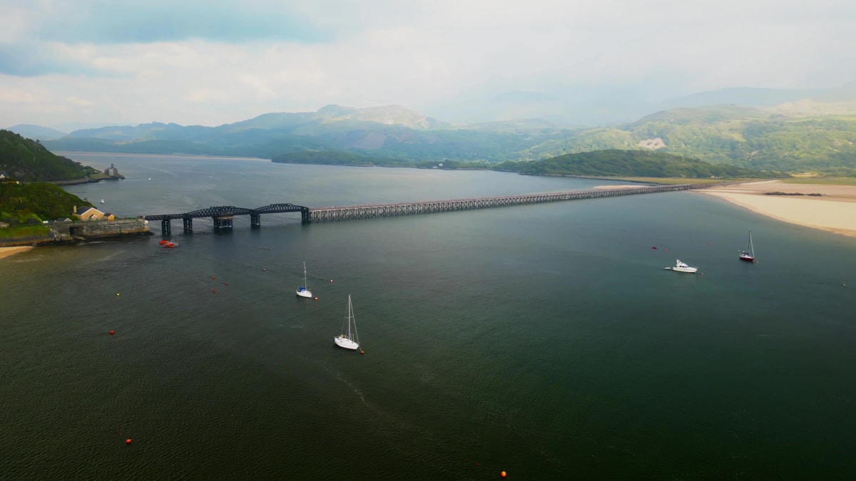 Aerial view of Barmouth Bridge spanning the Mawddach Estuary with Snowdonia hills behind, home water of Hurly Burly